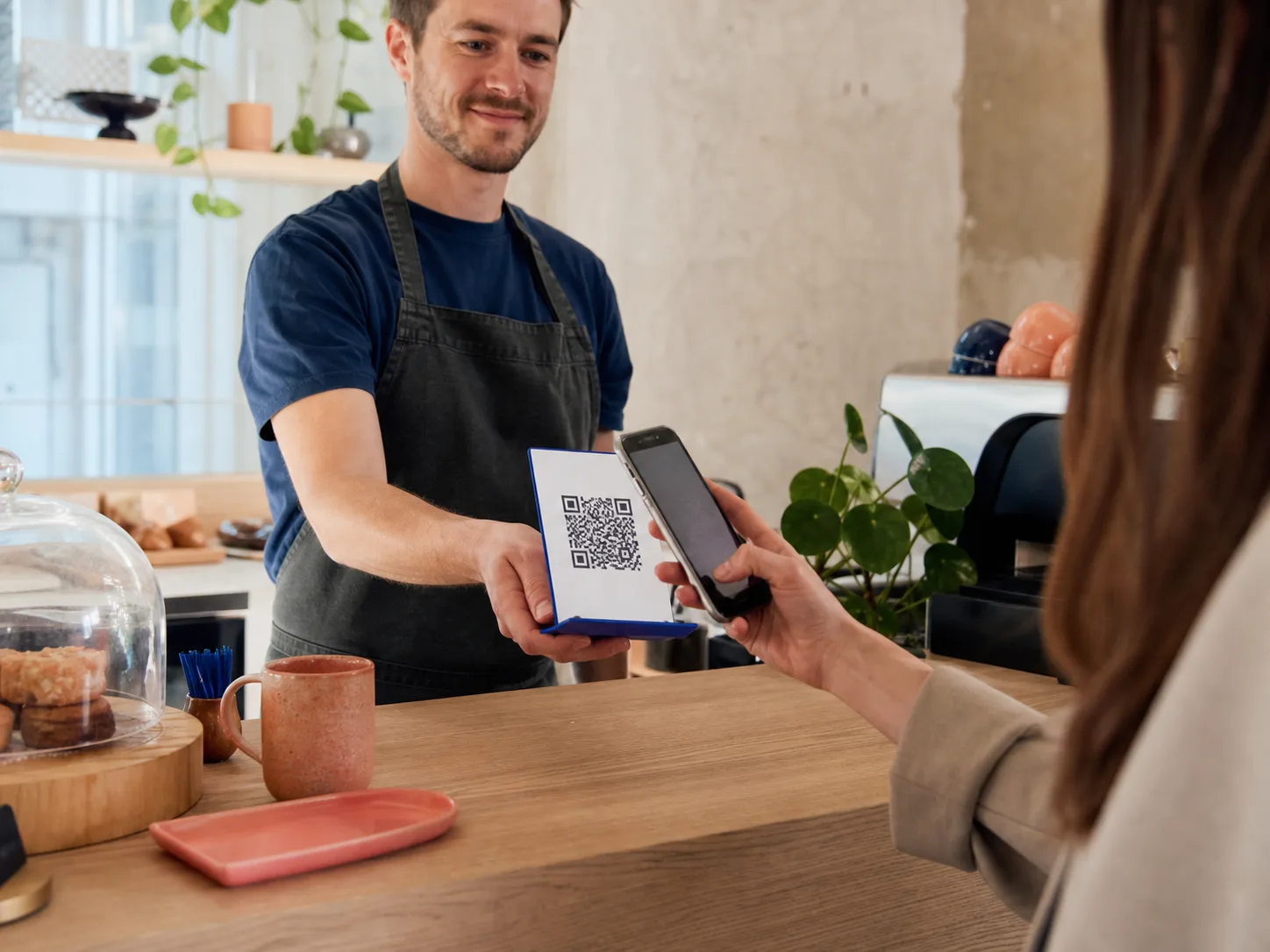 Une cliente scanne un QR code de paiement au comptoir d’un café